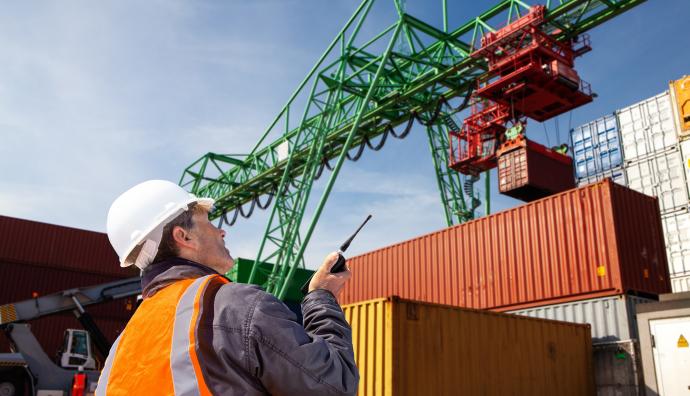 Mann mit Bauhelm und Walkie Talkie mit Containern im Hintergrund | Seacon Logistics